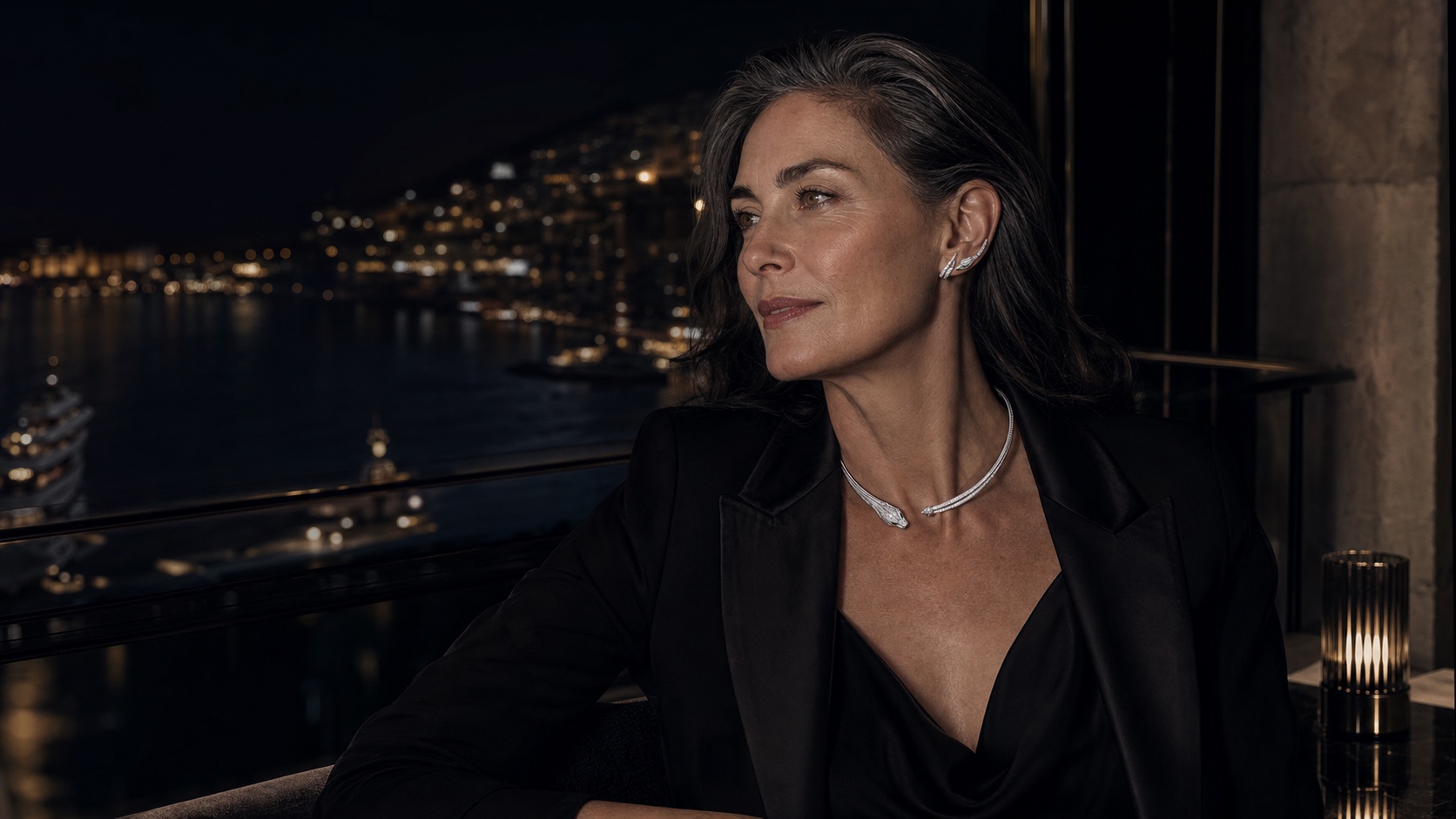 A woman with silver hair in low light before the harbour lights of Monaco, wearing the FELIS panther collar and ear climbers in white gold.
